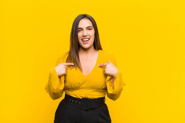 young pretty woman feeling happy, surprised and proud, pointing to self with an excited, amazed look isolated against orange wall - Fotoğraf, Görsel