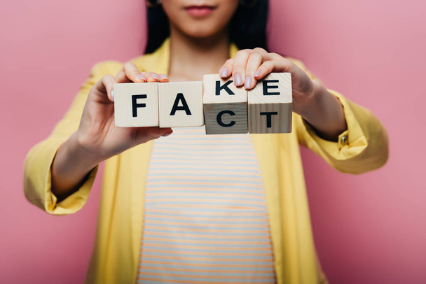 cropped view of asian woman holding wooden cubes with fake and fact lettering isolated on pink - Foto, Imagem