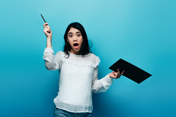 excited asian journalist in white blouse holding clipboard on blue background - Foto, immagini