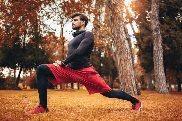 Hombre de deporte estirándose en el parque otoño, haciendo ejercicios
.  - Foto, Imagen