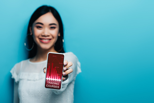 白いブラウスにアジアの女性の笑顔の選択的フォーカス青の背景に取引コースアプリでスマートフォンを保持 - 写真・画像