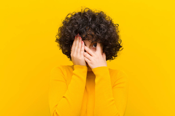 young pretty afro woman covering face with hands, peeking between fingers with surprised expression and looking to the side - Fotografie, Obrázek