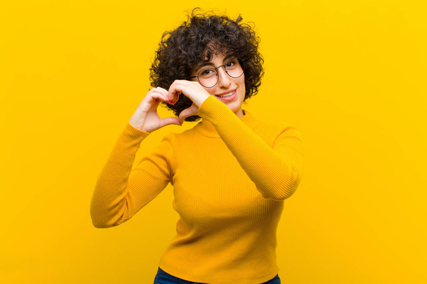 young pretty afro woman smiling and feeling happy, cute, romantic and in love, making heart shape with both hands - Foto, immagini