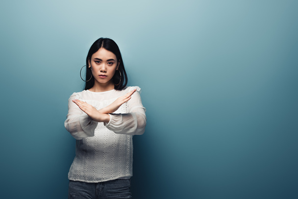 расстроен брюнетка азиатская женщина показывает стоп-жест на синем фоне
 - Фото, изображение