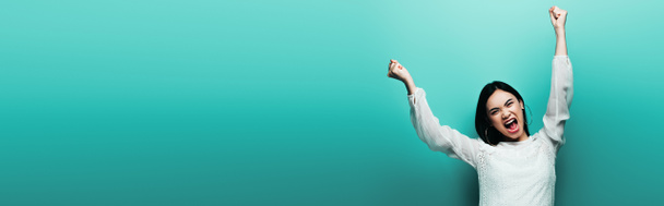 angry happy brunette asian woman yelling on turquoise background, panoramic shot - Photo, Image