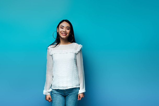 happy brunette asian woman on blue background - Fotó, kép