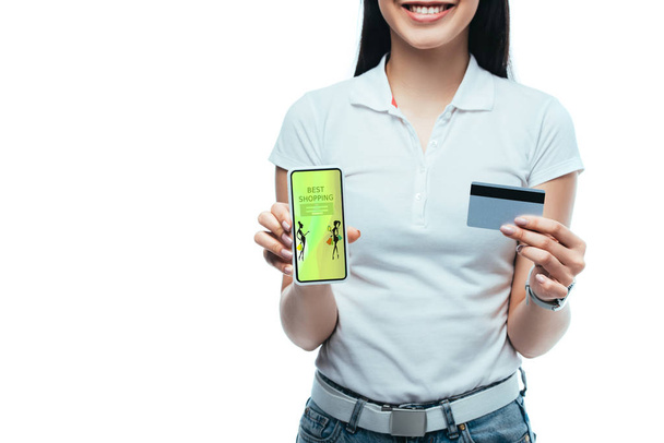 cropped view of smiling brunette asian girl holding credit card and smartphone with best shopping app isolated on white - Photo, Image