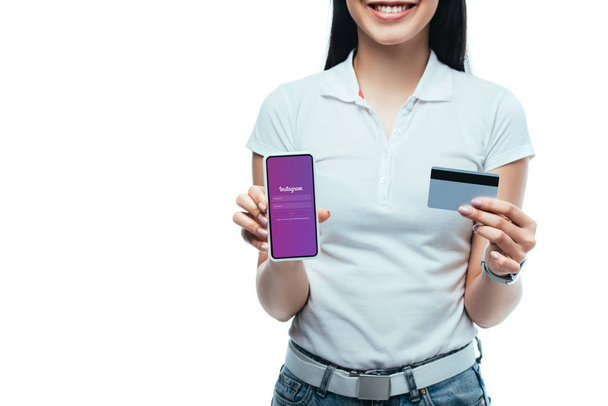 KYIV, UKRAINE - JULY 15, 2019: cropped view of smiling brunette asian girl holding credit card and smartphone with Instagram app isolated on white - Photo, image
