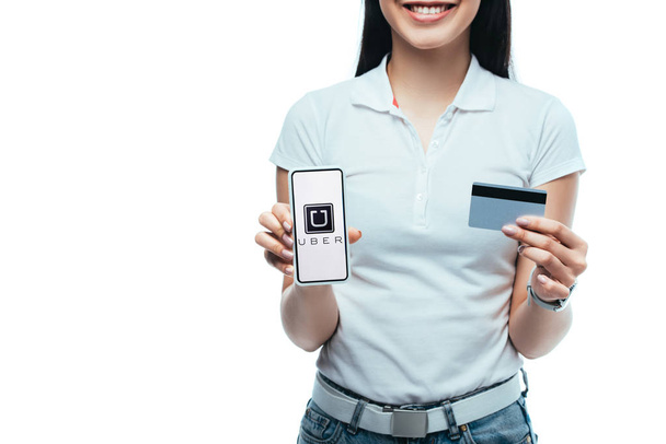 KYIV, UKRAINE - JULY 15, 2019: cropped view of smiling brunette asian girl holding credit card and smartphone with uber app isolated on white - Fotó, kép