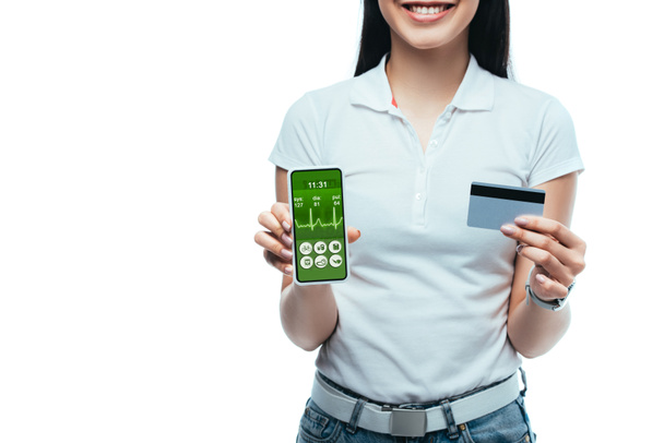 rajattu näkymä hymyilevä brunette aasialainen tyttö tilalla luottokortti ja älypuhelin terveydenhuollon app eristetty valkoinen
 - Valokuva, kuva