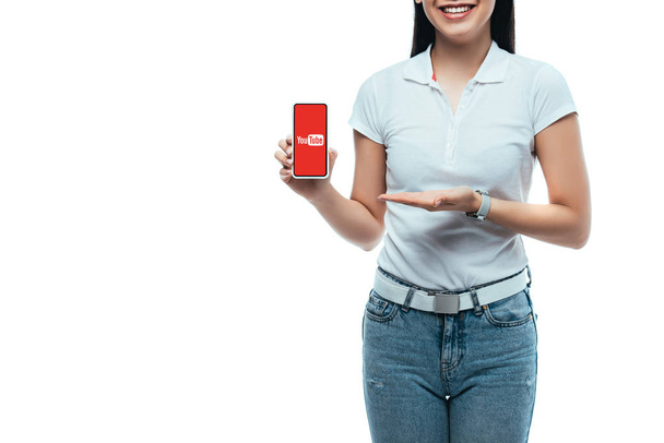 KYIV, UKRAINE - JULY 15, 2019: cropped view of happy brunette asian woman presenting smartphone with youtube app isolated on white - Foto, afbeelding