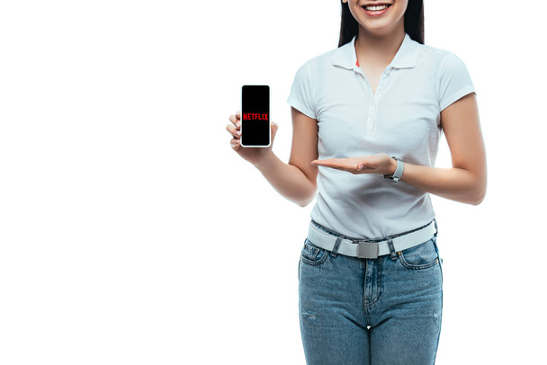 KYIV, UKRAINE - JULY 15, 2019: cropped view of happy brunette asian woman presenting smartphone with netflix app isolated on white - Foto, Bild