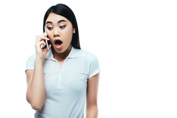 meglepett vonzó ázsiai lány nyitott szájjal beszél okostelefon elszigetelt fehér - Fotó, kép