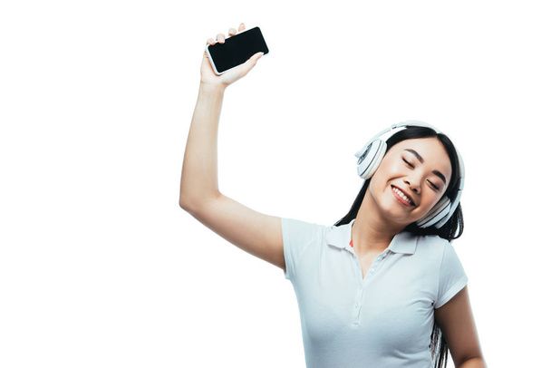 souriant attrayant asiatique fille dans casque tenant smartphone avec écran vide isolé sur blanc
 - Photo, image