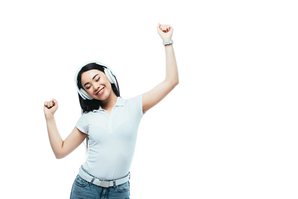 усміхнена приваблива азіатська дівчина танцює в навушниках ізольована на білому
 - Фото, зображення