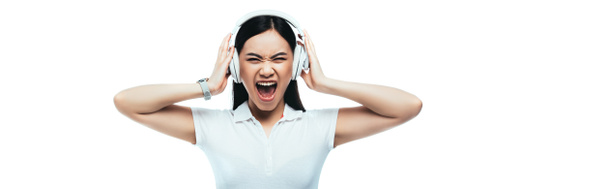 angry attractive asian girl screaming in headphones isolated on white, panoramic shot - Zdjęcie, obraz