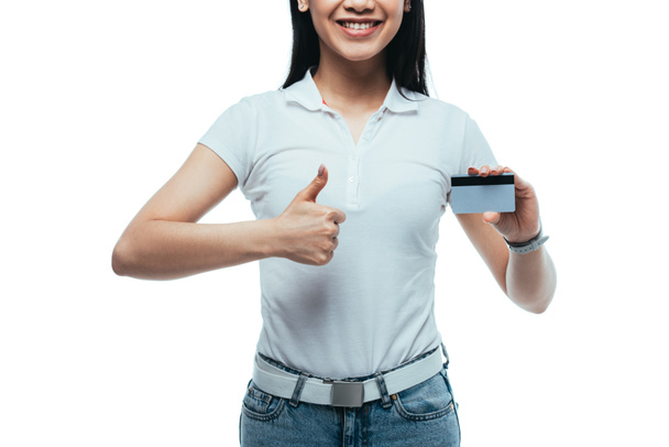 καλλιεργημένη άποψη της ευτυχούς ελκυστική ασιατική κορίτσι κρατώντας πιστωτική κάρτα και δείχνοντας τον αντίχειρα προς τα επάνω απομονώνονται σε λευκό - Φωτογραφία, εικόνα