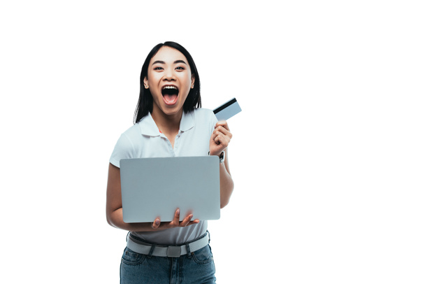excitado atractivo asiático chica con boca abierta celebración de tarjeta de crédito y portátil aislado en blanco
 - Foto, imagen
