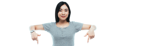 笑顔のアジア系の女の子が指を下に向けて白いパノラマのショットで隔離され - 写真・画像