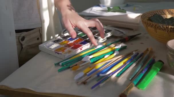 umělec zaměstnání, ženské malířské ruce vybrat štětec v blízkosti palety barev pro kreslení v ateliéru umění detailní - Záběry, video