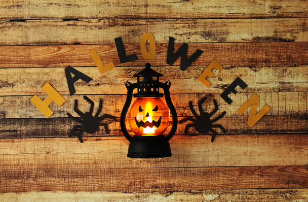 国民の祝日ハロウィンのためのシンプルな装飾。提灯の周りに黒と黄色の紙と黒のクモから作られ、ジャック・オ・ランタンの恐ろしい笑顔を形成しています。木製ボード上のハッピーハロウィン - 写真・画像