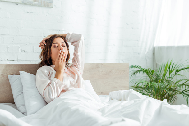 attractive woman in pajama with closed eyes yawning at morning  - Foto, Imagen