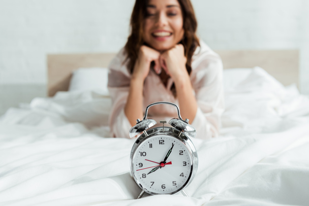 selective focus of attractive woman looking at alarm clock at morning  - 写真・画像