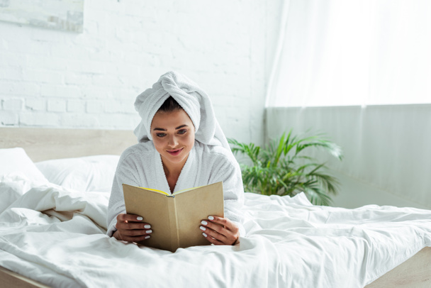 attractive woman in towel and bathrobe reading book at morning  - Fotografie, Obrázek