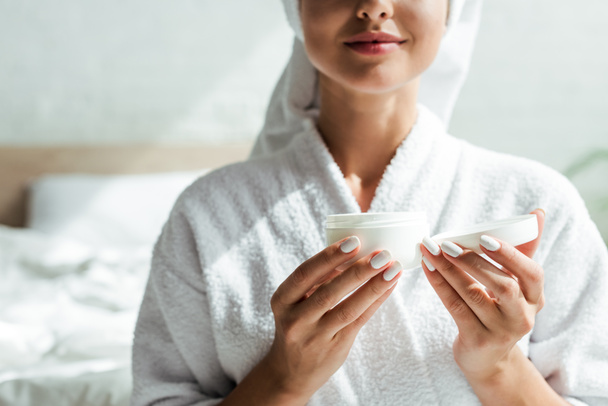cropped view of woman in bathrobe holding cosmetic cream at morning  - Фото, зображення