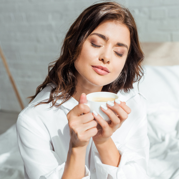 attractive woman in white shirt with closed eyes holding cup at morning  - Foto, immagini