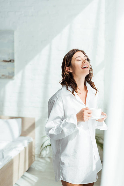 attractive woman in white shirt smiling and holding cup at morning  - 写真・画像