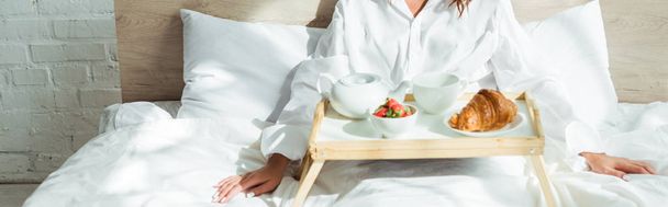 panorámás felvétel egy fehér inges nőről, aki az ágyban reggelizik reggel  - Fotó, kép