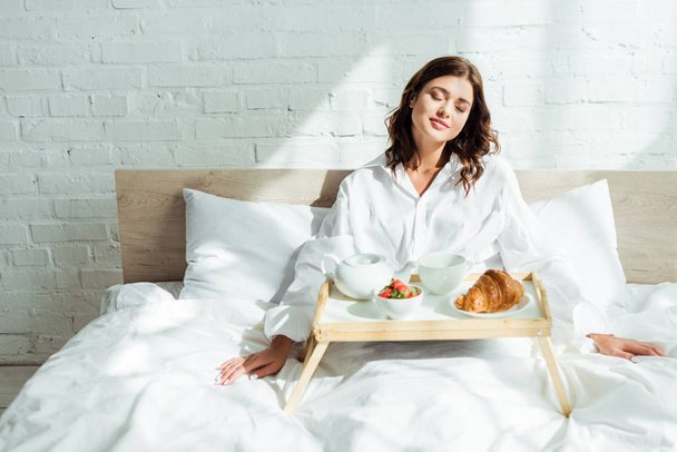 attractive woman in white shirt having breakfast in bed at morning  - Photo, Image