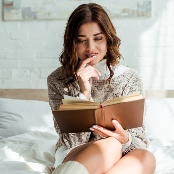 attractive woman in grey sweater reading book at morning  - Фото, изображение