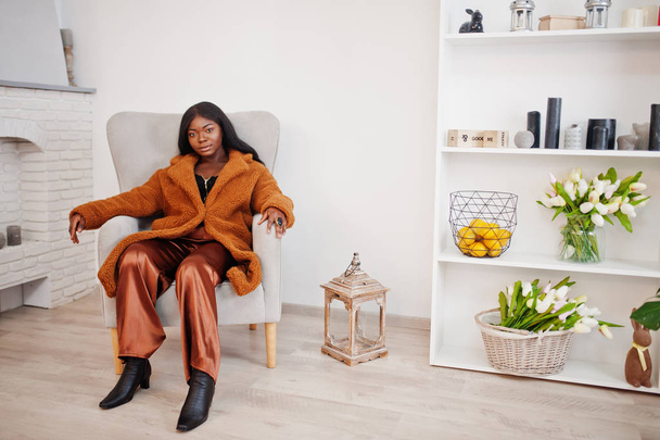 Stylish african american woman in orange coat posed at room sitt - Fotografie, Obrázek