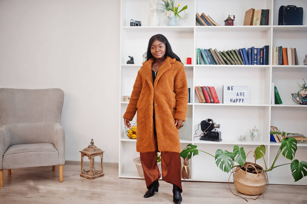 Stylish african american woman in orange coat posed at room in f - Foto, afbeelding