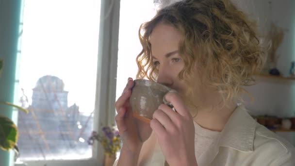 coffee break of happy smiling painter woman with cup hot drink enjoying creative process against sunlit window - Séquence, vidéo