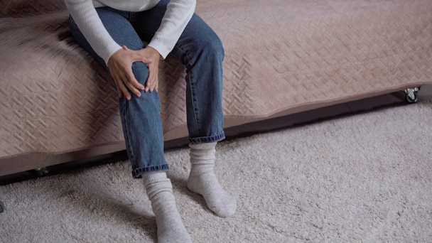 mujer joven sintiendo dolor de rodilla mientras se levanta del sofá
 - Imágenes, Vídeo