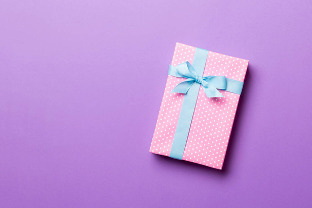 verpakt Kerstmis of andere met de hand gemaakte vakantie cadeau in papier met blauw lint op paarse achtergrond. Aanwezig doos, decoratie van geschenk op gekleurde tafel, bovenaanzicht met kopieerruimte - Foto, afbeelding