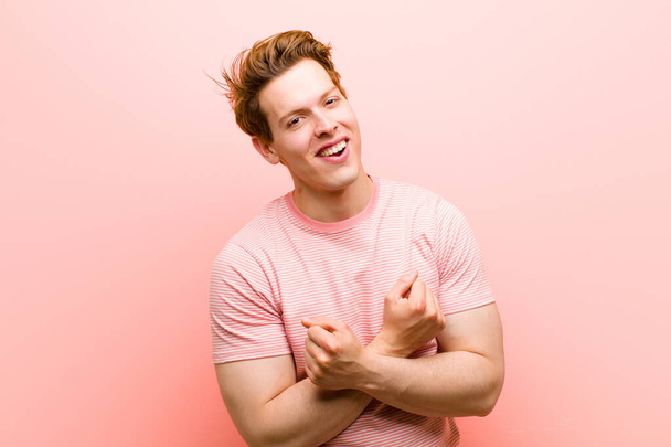 young red head man smiling cheerfully and celebrating, with fists clenched and arms crossed, feeling happy and positive against pink wall - Foto, imagen