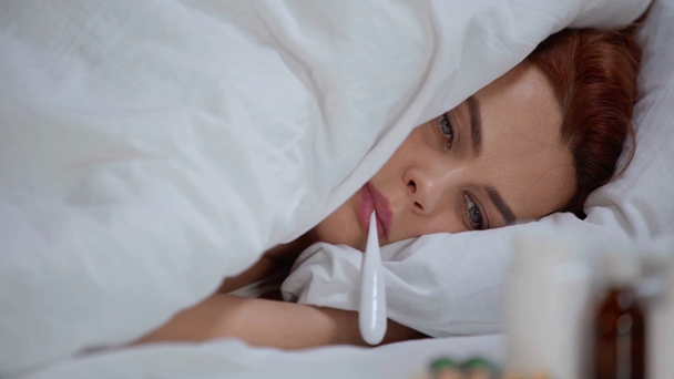 sairas nainen makaa peiton alla ja mittaa lämpötilaa lämpömittarilla
 - Materiaali, video
