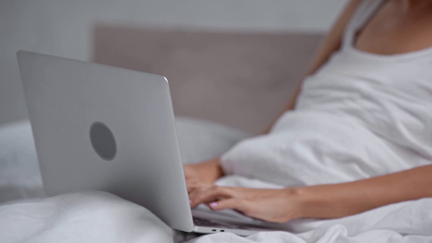 cropped view of woman sitting in bed and using laptop - Video, Çekim