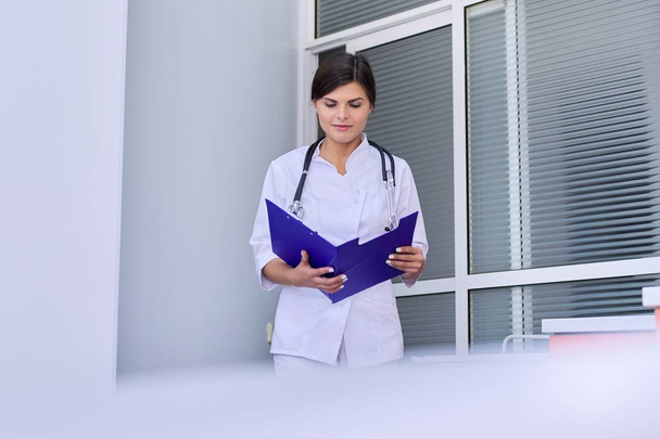 Female doctor with stethoscope reading medical documents in clipboard folder - Photo, Image