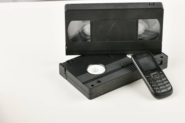 Retro objecten op een witte achtergrond. telefoon met drukknop en videocassette. Analoge mediatechnologie uit het verleden. Kopieerruimte - Foto, afbeelding