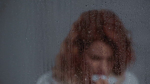 chora kobieta kaszle w pobliżu szyby z kroplami deszczu - Materiał filmowy, wideo