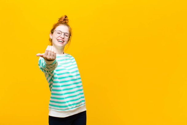 junge Frau mit rotem Kopf, die sich glücklich, erfolgreich und zuversichtlich fühlt, vor einer Herausforderung steht und sagt: Her damit! oder begrüßen Sie gegen orangefarbene Wand - Foto, Bild