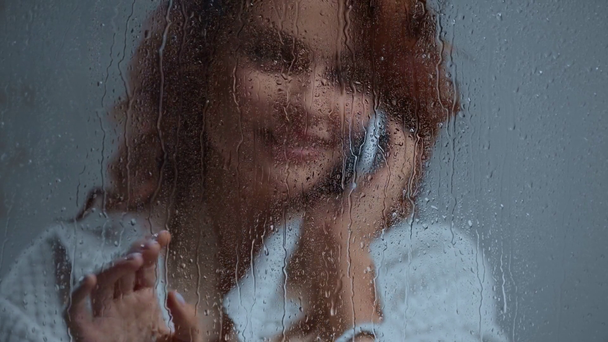 vidám nő beszél okostelefon üvegablak közelében esőcseppek - Felvétel, videó