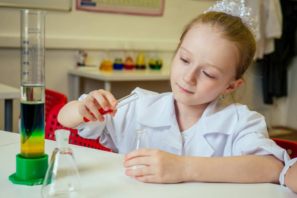 clever blonde school girl chemist in eyeglasses and white medical gown making science experiments chemistry ,mixing different chemical solutions in laboratory classroom - Foto, Bild