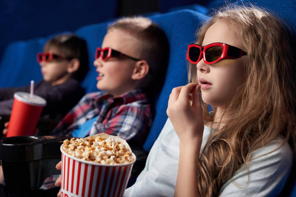 View from side of girl wearing 3d glasses eating popcorn - Foto, Imagem