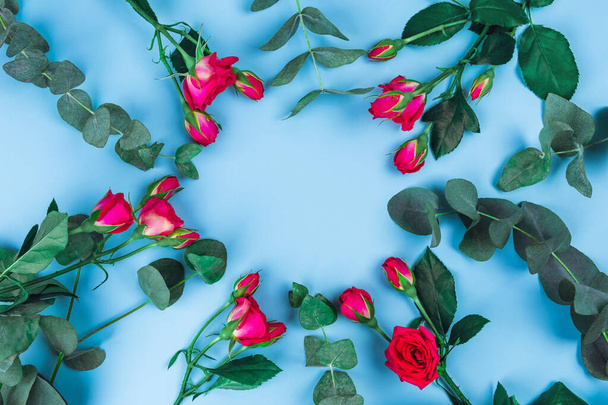 Beautiful sprigs of eucalyptus and roses on blue background, top view. - 写真・画像